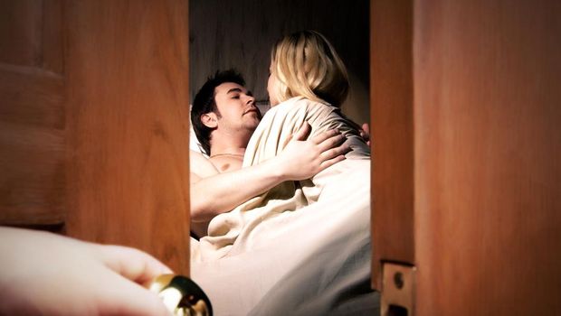 Couple lying in bed while someone is watching in front of the door