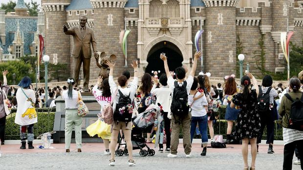 Visitors wave to Disney characters performing at Tokyo Disneyland in Urayasu, near Tokyo, Wednesday, July 1, 2020. Tokyo Disneyland reopened for the first time in four months after suspending operations due to coronavirus concerns. (Kyodo News via AP)