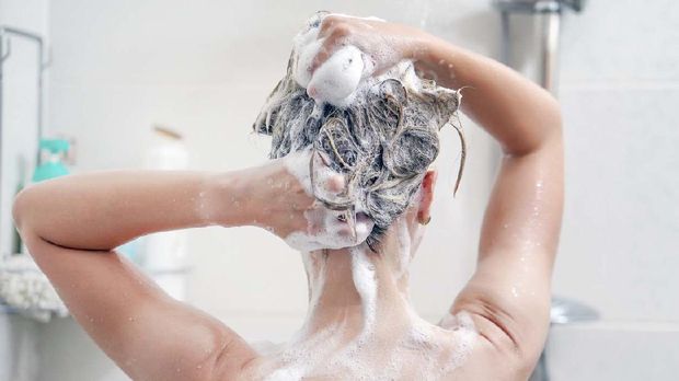 Woman washes her hair with shampoo in bathroom. Woman washing her hair with a lot of foam inside a shower. Back view of young woman washing her hair.