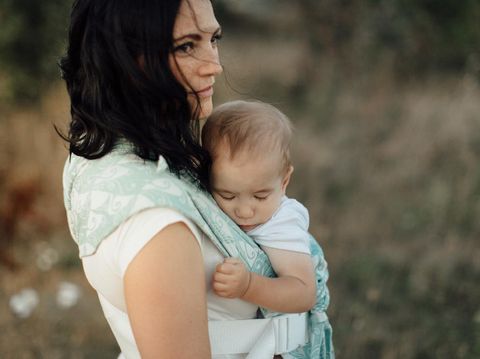 Portrait of woman carrying her little baby in sling in the fields on summer day.