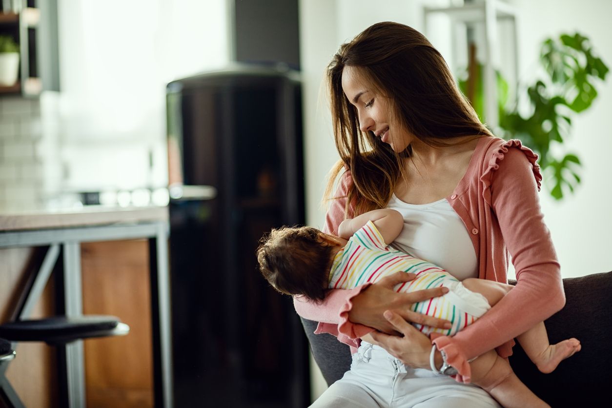 Smiling mother breastfeeding her baby daughter while being at home.