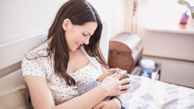 Smiling mother breastfeeding her baby daughter while being at home.