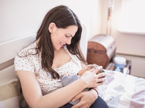 Smiling mother breastfeeding her baby daughter while being at home.