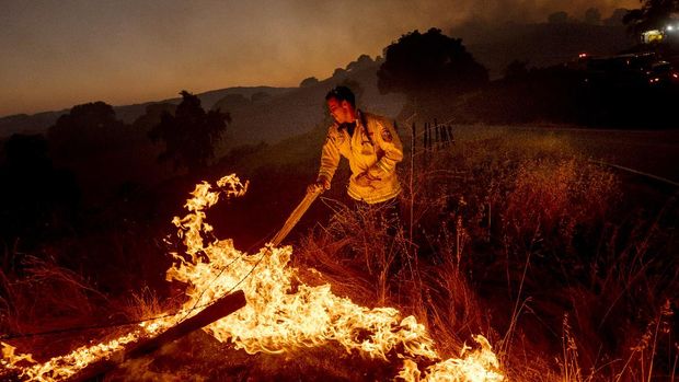 A firefighter moves a fence post while battling the Crews Fire near Gilroy, Calif., on Sunday, July 5, 2020. (AP Photo/Noah Berger)