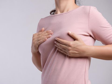 Woman hand checking lumps on her breast for signs of breast cancer on gray background. Healthcare concept.