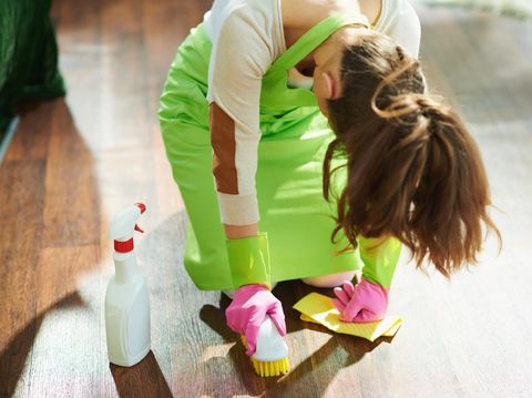 tired modern 40 years old housewife in green apron and pink rubber gloves with spray bottle of cleaning supplies, brush and yellow wipe wet cleaning floor in the modern house in sunny day.