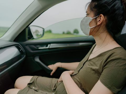 Young pregnant woman behind the steering wheel having contractions