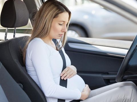 Young pregnant woman behind the steering wheel having contractions