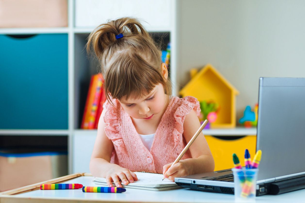 Beautiful little girl writing homework using notebook for distance learning in the kids room. Distance online learning concept.