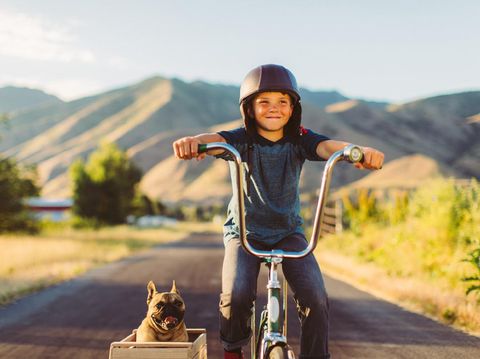 A young boy with vintage clothing and motorcycle helmet rides his stingray bicycle with his pet and best friend French Bulldog riding along in a side car in Utah, USA. Sometimes a road trip journey with your best friend and some fresh air in your face is the best medicine for the soul.