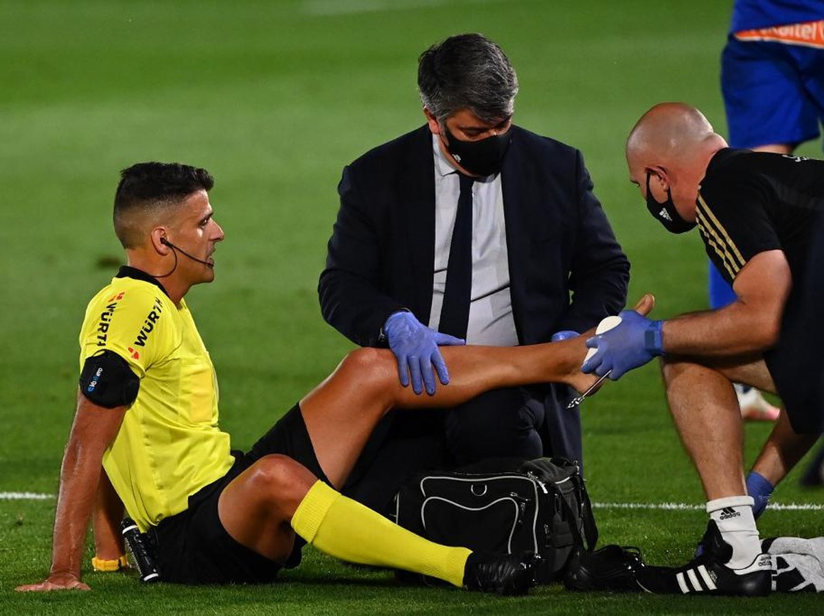 Wasit Jesus Gil Manzano mendapat bantuan perawatan dari tim medis Real Madrid di laga pekan ke-35 melawan Deportivo Alaves, Sabtu (11/7/2020) dini hari WIB. (Foto: GABRIEL BOUYS / AFP)