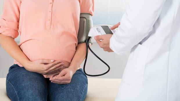 Midsection of male doctor checking pregnant woman's blood pressure in hospital