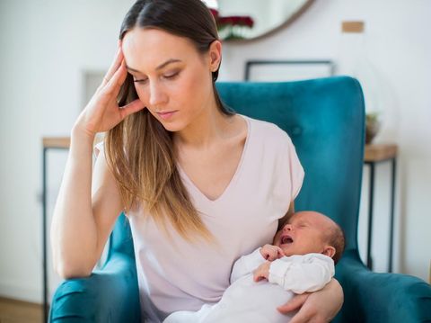 Stressed Mother Holding Crying Baby Suffering From Post Natal Depression At Home