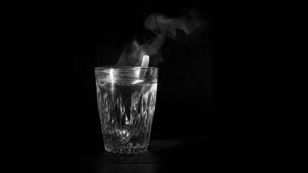 Transparent glass cup with swell the boiling water into it. The vapor from the top. Black background. Space for text.