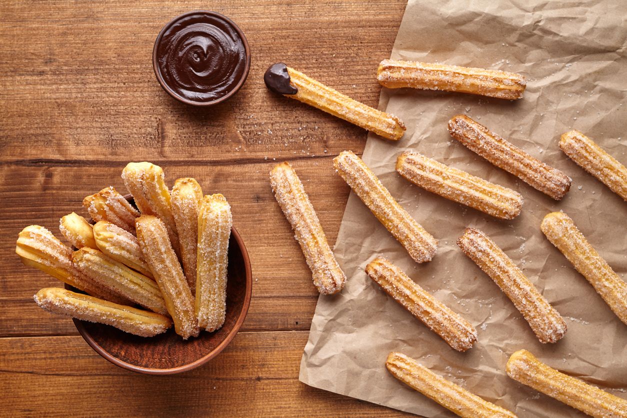 churros - Traditional Spanish and Mexican dessert on a white plate with chocolate sauce on an old grey rustic wooden table, horizontal view from above, close-up, flatlay
