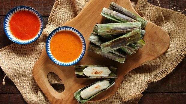 Otak-otak, the traditional snack of grilled fish cake from Jakarta. The fish cake is wrapped in banana leaf then grilled on a charcoal grill. The fish cakes are arranged on a bamboo basket with one of the cakes shown unwrapped.