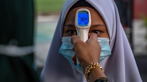 Ilustrasi -- Siswa Malaysia kembali ke sekolah di tengah pandemi virus Corona A high school teacher checks the temperature of a student on the first day after being reopened following restrictions to halt the spread of the COVID-19 coronavirus in Kuala Lumpur on June 24, 2020. (Photo by Mohd RASFAN / AFP)