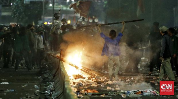 Massa aksi membubarkan diri pukul 20:15 WIB dengan di kawal aparat, massa sempat melakukan pembakaran atribut dan meninggalkan coretan di tembok pembatas jalan usai melakukan aksi menolak Omnibus Law RUU Cipta Lapangan Kerja menggelar aksi di sisi kiri pintu gerbang DPR RI, Jakarta, Kamis (16/7). Akibat aksi massa lalu-lintas di jalan tol depan gedung DPR RI sempat terhambat CNN Indonesia/Andry Novelino