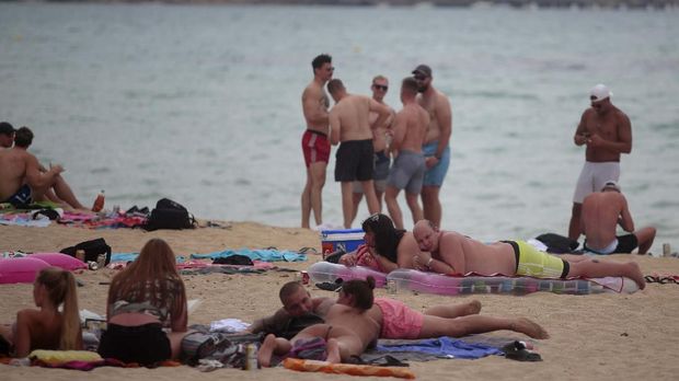 Tourists enjoy the beach at the Spanish Balearic island of Mallorca, Spain, Thursday, July 16, 2020. In a move designed to stop the spread of the new coronavirus and shake off the region's reputation as a party hub, regional authorities in the Balearic Islands ordered the closure from Thursday of all establishments along Mallorca's 
