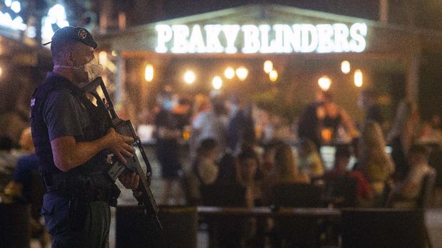 A Guardia Civil officer holds his weapons as tourists stand in a bar at the resort of Magaluf on the Spanish Balearic island of Mallorca, Spain, Thursday morning, July 16, 2020. Authorities in Spain's Balearic Islands are pulling the plug on endless drunken nights to the beat of techno music by closing bars and nightclubs in beachfront areas popular with young and foreign visitors. (AP Photo/Joan Mateu)