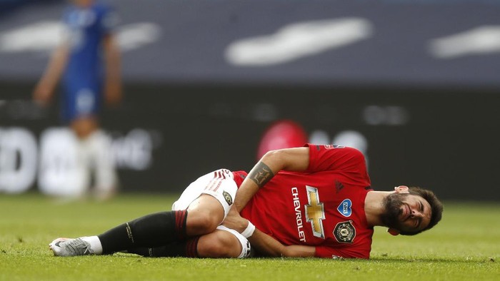 Manchester Uniteds Bruno Fernandes grimaces after getting injured during the English FA Cup semifinal soccer match between Chelsea and Manchester United at Wembley Stadium in London, England, Sunday, July 19, 2020. (AP Photo/Alastair Grant, Pool)
