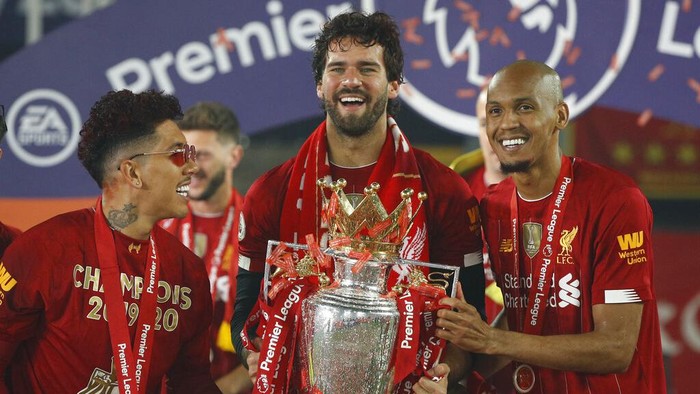 Liverpools Roberto Firmino, left, Liverpools goalkeeper Alisson, center, and Liverpools Fabinho, celebrate with the English Premier League trophy following its presentation to the team for winning the EPL 2019-2020 season after the soccer match between Liverpool and Chelsea at Anfield Stadium in Liverpool, England, Wednesday, July 22, 2020. Liverpool won the match 5-3. (Phil Noble/Pool via AP)