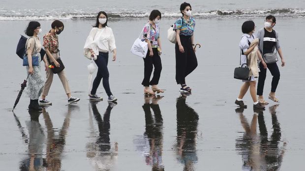 People wearing face masks to protect against the spread of the new coronavirus walk on a beach on a national holiday in Fujisawa, Kanagawa prefecture, near Tokyo, Thursday, July 23, 2020. (AP Photo/Koji Sasahara)