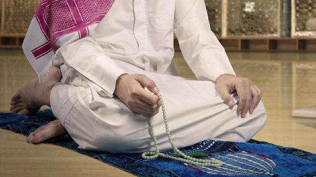 Close up of devout muslim person wearing islamic clothes and using beads to dhikr in the mosque