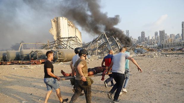Ledakan di Beirut, Libanon Civilians carry a victim at the explosion scene that hit the seaport, in Beirut Lebanon, Tuesday, Aug. 4, 2020. Massive explosions rocked downtown Beirut on Tuesday, flattening much of the port, damaging buildings and blowing out windows and doors as a giant mushroom cloud rose above the capital. Witnesses saw many people injured by flying glass and debris. (AP Photo/Hussein Malla)