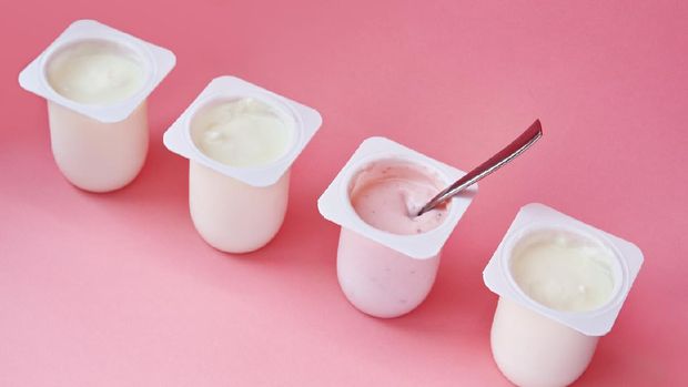 Four yogurts in white plastic cups on pink background with copy space. Strawberry pink yoghurt with spoon in it. Minimal style. Concept of better choice.