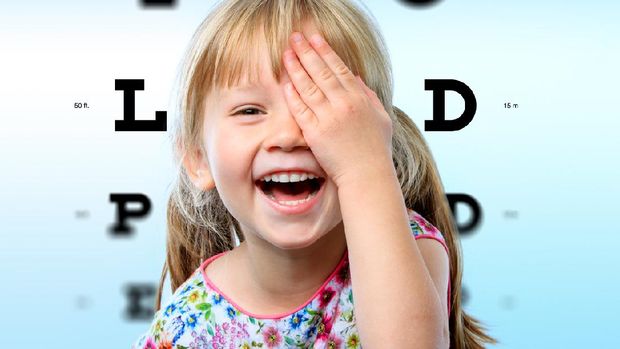 Close up face portrait of happy girl having fun at vision test.Conceptual image with girl closing one eye with hand and block letter eye chart in background.