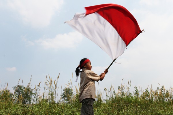 Beautiful young mother with her daughter celebrating indonesia independence day by raising flag under the sunset sky