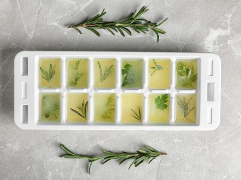 Ice cube tray with herbs frozen in oil and fresh rosemary on grey background, flat lay