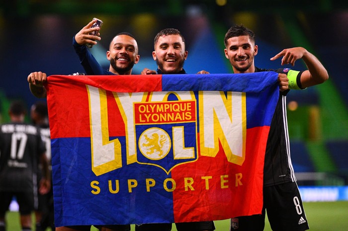 LISBON, PORTUGAL - AUGUST 15: Memphis Depay, Rayan Cherki and Houssem Aouar of Olympique Lyon celebrate with a supporters flag following their teams victory in the UEFA Champions League Quarter Final match between Manchester City and Lyon at Estadio Jose Alvalade on August 15, 2020 in Lisbon, Portugal. (Photo by Franck Fife/Pool via Getty Images)