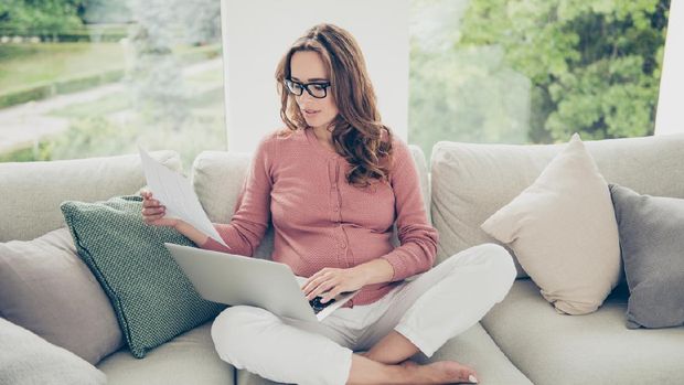 Above high angle view of nice lovely beautiful minded serious pregnant curly-haired mom in casual wear sitting on sofa, couch, divan, working remotely, lotus pose, white light interior room