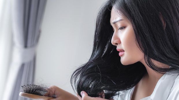 Attractive Asian woman serious about her brush for presentation hair loss problem and looking at comb