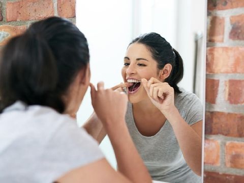 Shot of a beautiful young woman flossing her teeth in the bathroom mirror