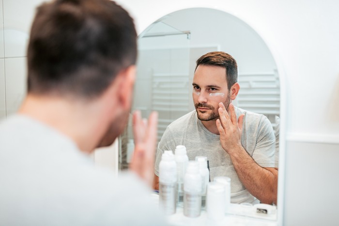 Handsome man applying face cream in the bathroom.