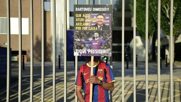 An FC Barcelona fan holds a placard calling for the resignation of club president Josep Maria Bartomeu and replacing him with Barcelonas Spanish defender Gerard Pique as fans gather outside the Camp Nou stadium in Barcelona on August 27, 2020 after Barcelonas Argentinian forward Lionel Messi announced his desire to leave the club. - Lionel Messis bombshell request to leave Barcelona is expected to spark a legal battle over a multi-million-dollar buy-out clause but also raises the question of which club could afford him in the heat of the coronavirus pandemic. (Photo by Pau BARRENA / AFP)