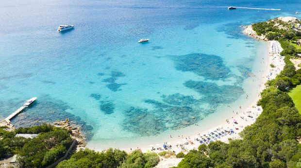 Emerald Coast, Sardinia View from above, stunning aerial view of a beautiful beach full of colored beach umbrellas and people swimming in a turquoise clear water. Capriccioli Beach, Costa Smeralda, Sardinia, Italy.