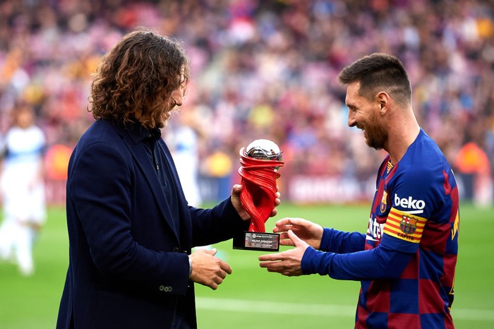 BARCELONA, SPAIN - DECEMBER 21: Lionel Messi of FC Barcelona receives the trophy as best player of November in the Spanish La Liga from Carles Puyol  before the La Liga match between FC Barcelona and Deportivo Alaves at Camp Nou on December 21, 2019 in Barcelona, Spain. (Photo by Alex Caparros/Getty Images)