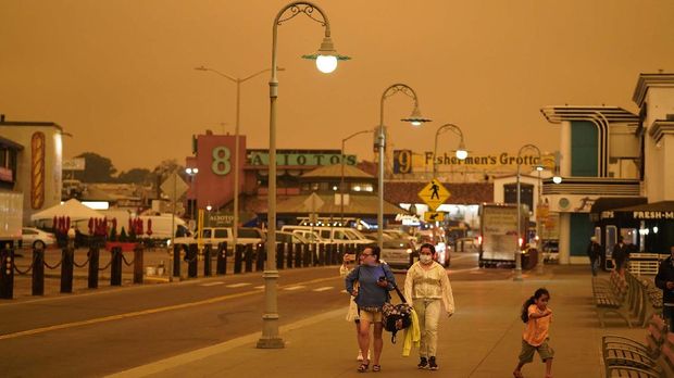 Under darkened skies from wildfire smoke, people walk at Fisherman's Wharf Wednesday, Sept. 9, 2020, in San Francisco. People from San Francisco to Seattle woke Wednesday to hazy clouds of smoke lingering in the air, darkening the sky to an eerie orange glow that kept street lights illuminated into midday, all thanks to dozens of wildfires throughout the West. The picture was taken in the middle of the day at 1:01 p.m. (AP Photo/Eric Risberg)
