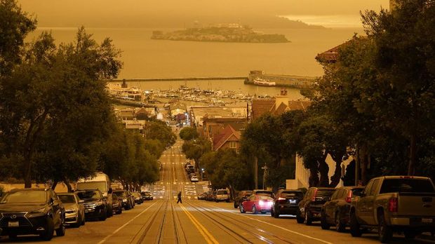 Under darkened skies from wildfire smoke, a man crosses Hyde Street with Alcatraz Island and Fisherman's Wharf in the background Wednesday, Sept. 9, 2020, in San Francisco. People from San Francisco to Seattle woke Wednesday to hazy clouds of smoke lingering in the air, darkening the sky to an eerie orange glow that kept street lights illuminated into midday, all thanks to dozens of wildfires throughout the West. The picture was taken in the middle of the day at 12:29 p.m. (AP Photo/Eric Risberg)