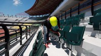 Seorang pekerja menyelesaikan pemasangan kursi single seat di tribun stadion.