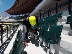 Seorang pekerja menyelesaikan pemasangan kursi single seat di tribun stadion.