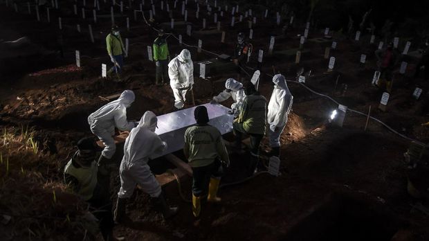 Petugas penggali makam jenazah COVID-19 menurunkan peti ke dalam liang lahat di komplek pemakaman Pondok Ranggon. ANTARA FOTO/Muhammad Adimaja