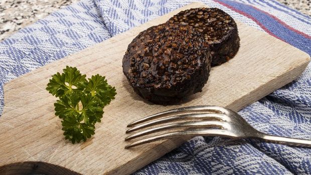 grilled irish black pudding made with oatmeal on a wooden board with knife and parsley