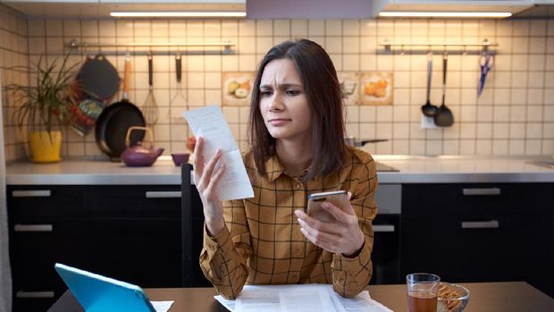 An attractive young housewife wears a shirt at home and examines gas and electricity bills. grimly considers spending this month and is under stress when checking accounts.