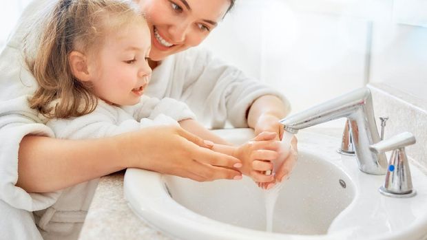 Cute little girl and her mother are washing hands under running water.