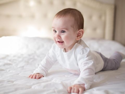 Cute little 10 months old baby lying on the bed and looking into the camera.